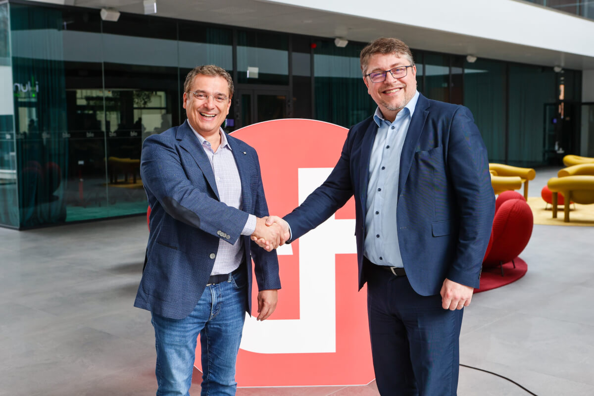 Two men shaking hands in front of a red sign representing Devoteam Cloud.